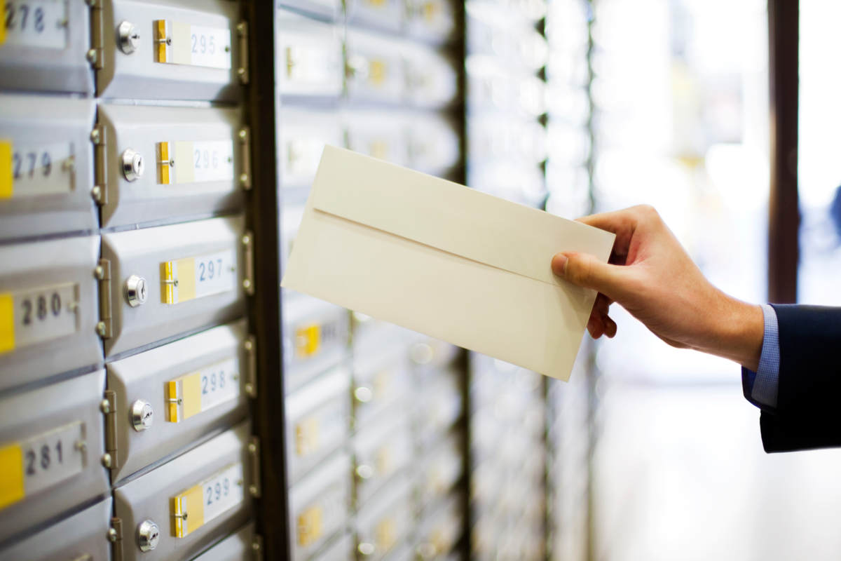 Sending or receiving mail, a hand holding a letter in front of mailboxes. Mailing lists related stock photo.