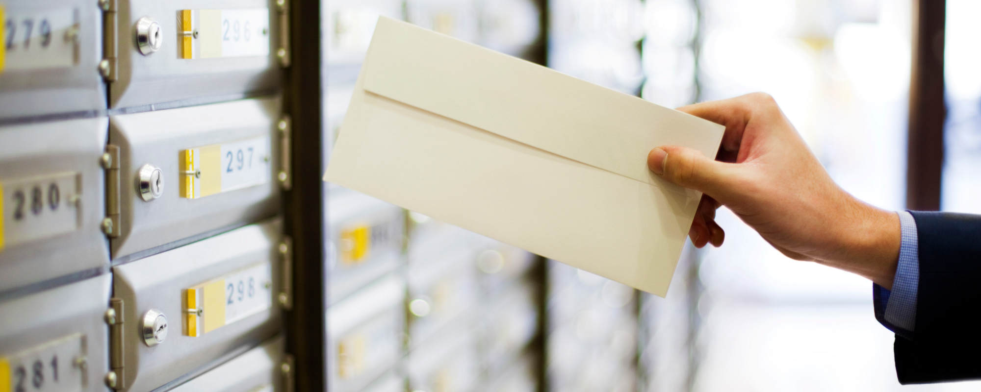 Sending or receiving mail, a hand holding a letter in front of mailboxes. Mailing lists related stock photo.